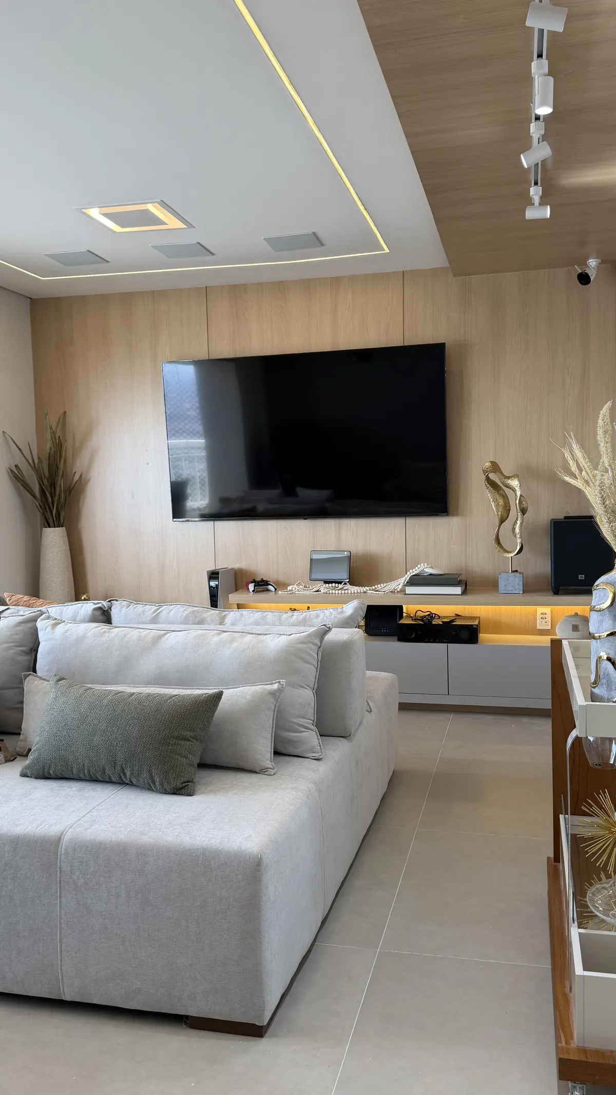 Sala de estar com sofá claro, painel de madeira com TV e forro com iluminação embutida