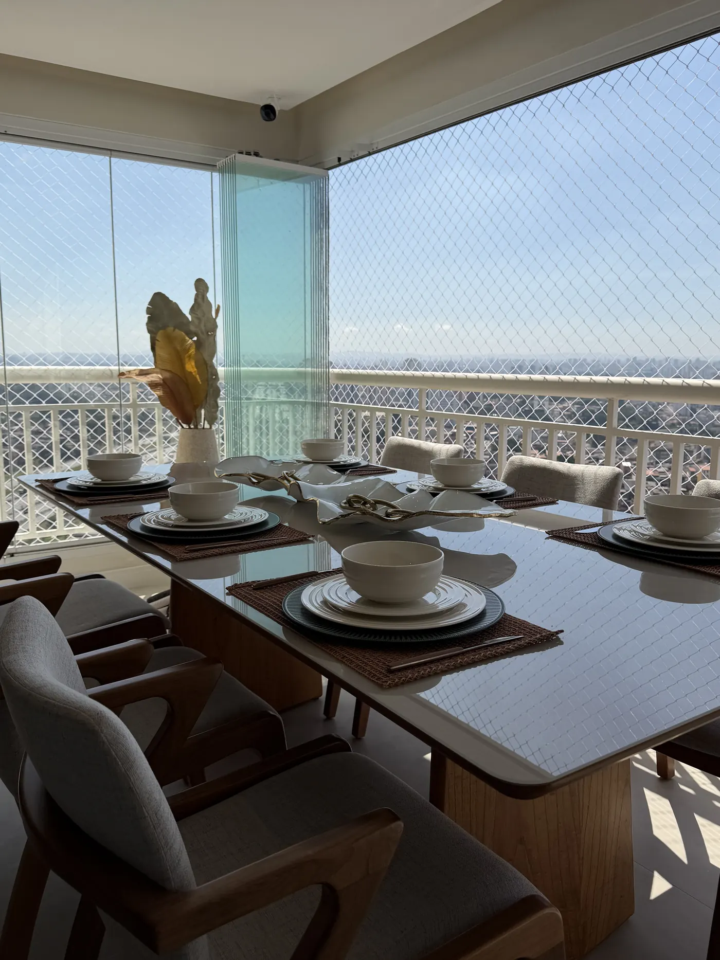 Varanda gourmet envidraçada com mesa de jantar posta e vista aberta para a cidade