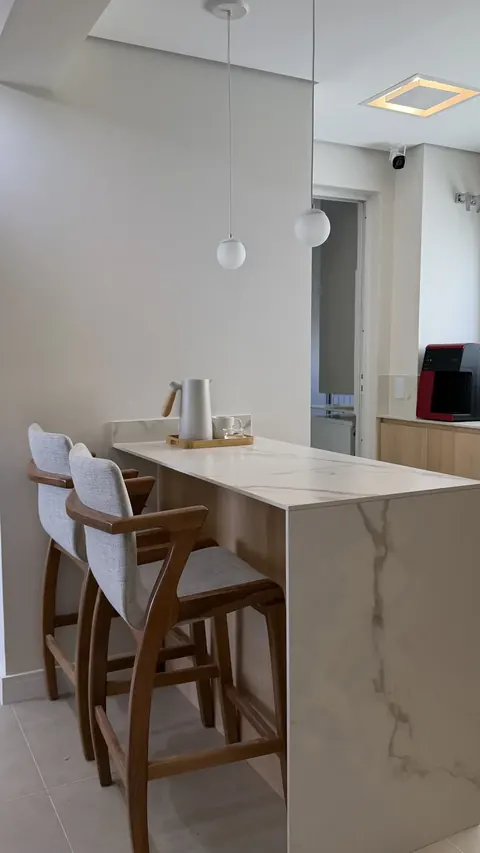 Bancada em pedra clara com banquetas estofadas e pendentes sobre ela