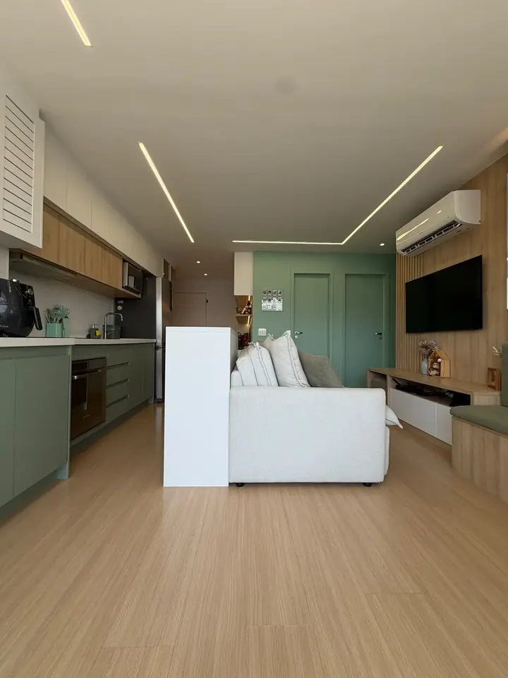 Sala de estar integrada à cozinha com marcenaria em madeira clara, parede verde, painel ripado com TV e iluminação em fita de LED no forro